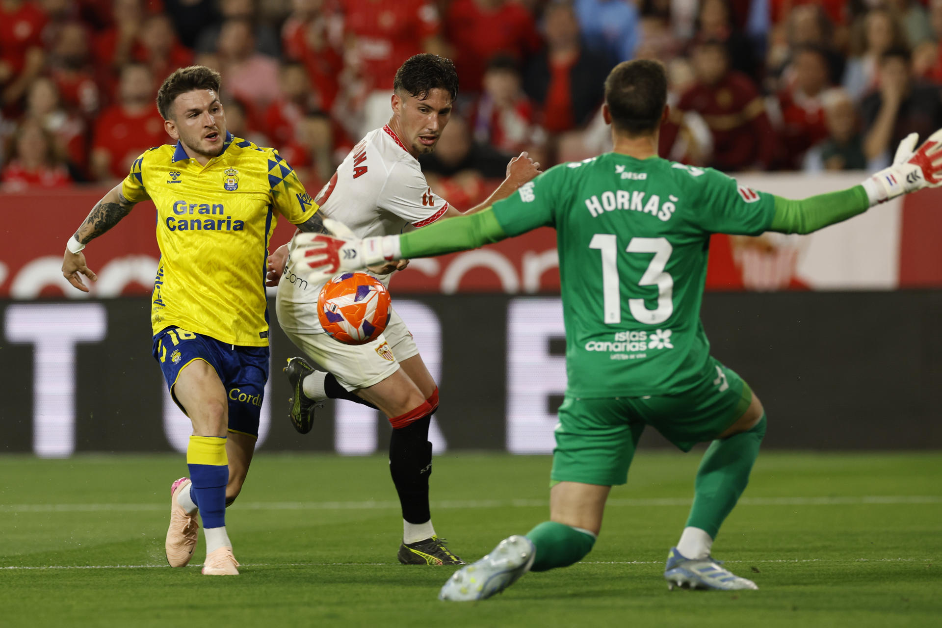 El ddefensa del Sevilla FC José Carmona (c) lucha el balón con Viti Álvarez (i), de la UD Las Palmas, durante el partido de la jornada 36 de LaLiga que Sevilla FC y UD Las Palmas disputan en el estadio Ramón Sánchez-Pizjuán. EFE/Julio Muñoz