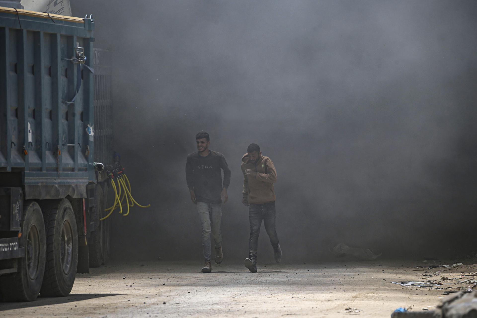 Palestinos corren para cubrirse mientras se eleva el humo tras un ataque aéreo israelí al oeste de la ciudad de Gaza, en la Franja de Gaza. EFE/MOHAMMED SABER