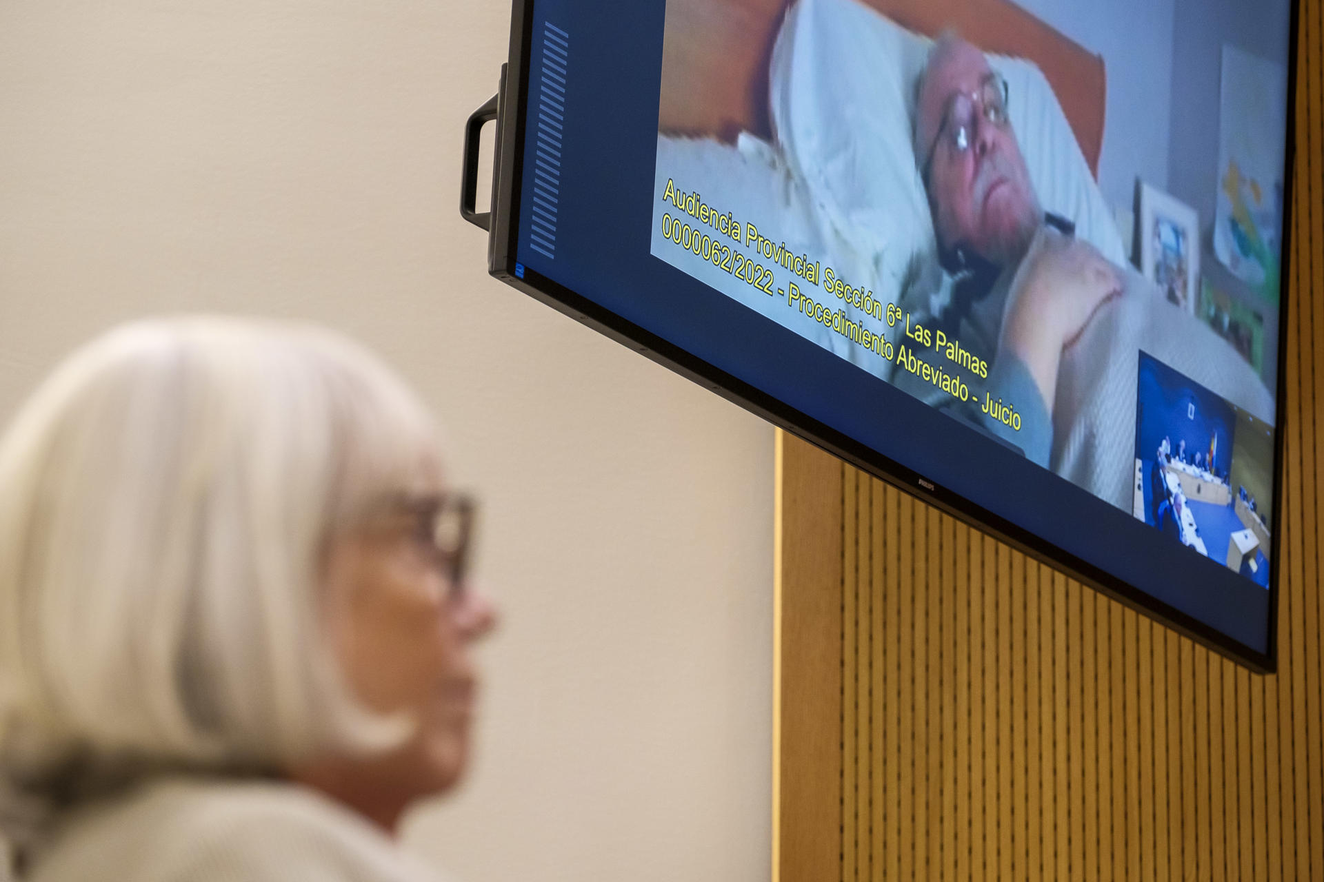 El empresario ruso afincado en Gran Canaria Vladimir Kokorev (en la pantalla) ha aceptado este lunes en la Audiencia de Las Palmas una condena de dos años y tres meses de cárcel -tiempo que ya ha cumplido en prisión preventiva- y 20 millones de euros de multa tras confesar que blanqueó 58 millones no declarados de sus negocios con Guinea Ecuatorial entre 1999 y 2012. En la imagen, la acusada Yulia Maleeva escucha desde la sala de vistas la conformidad de su esposo, que está enfermo. EFE/ Ángel Medina G.