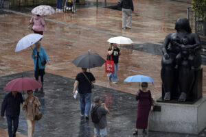 Viandantes con paraguas bajo la lluvia en la plaza de La Escandalera en Oviedo, este viernes. EFE/Paco Paredes