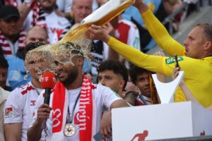 Linton Maina (izq.), del Colonia, pronuncia un discurso mientras se ducha con cerveza tras ganar el partido de la segunda división de la Bundesliga alemana entre el.FC Colonia y el.FC Kaiserslautern en Colonia, Alemania. EFE/EPA/CHRISTOPHER NEUNDORF