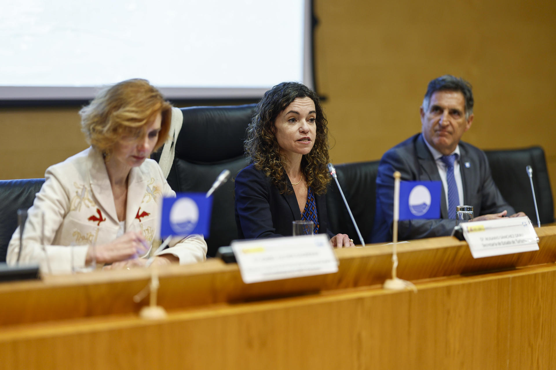 La secretaria de Estado de Turismo Rosario Sánchez Grau (c), la asesora del Secretario General para Sosteniblidad ONU Turismo Isabel Oliver Sagreras (i) y el presidente de ADEAC José Palacios Aguilar, durante el acto de la Asociación de Educación Ambiental y del Consumidor (Adeac) este martes en Madrid, que da a conocer la lista de playas, puertos y embarcaciones turísticas galardonadas con Bandera Azul 2025. EFE/ Rodrigo Jiménez