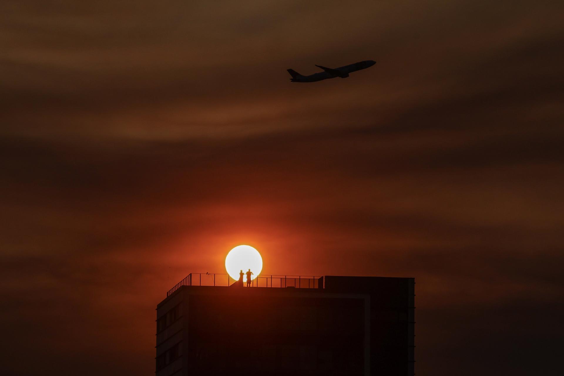 Una pareja observa la puesta de sol en lo alto de un edificio mientras un avión pasa cerca del Parque Tejo en Lisboa, Portugal, 05 de agosto de 2023. EFE/EPA/MIGUEL A. LOPES /