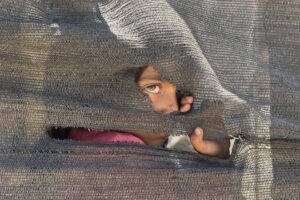 Una niña se asoma tras una tienda improvisada en el puerto en la Ciudad de Gaza, el 20 de mayo de 2025. EFE/ Ahmad Awad