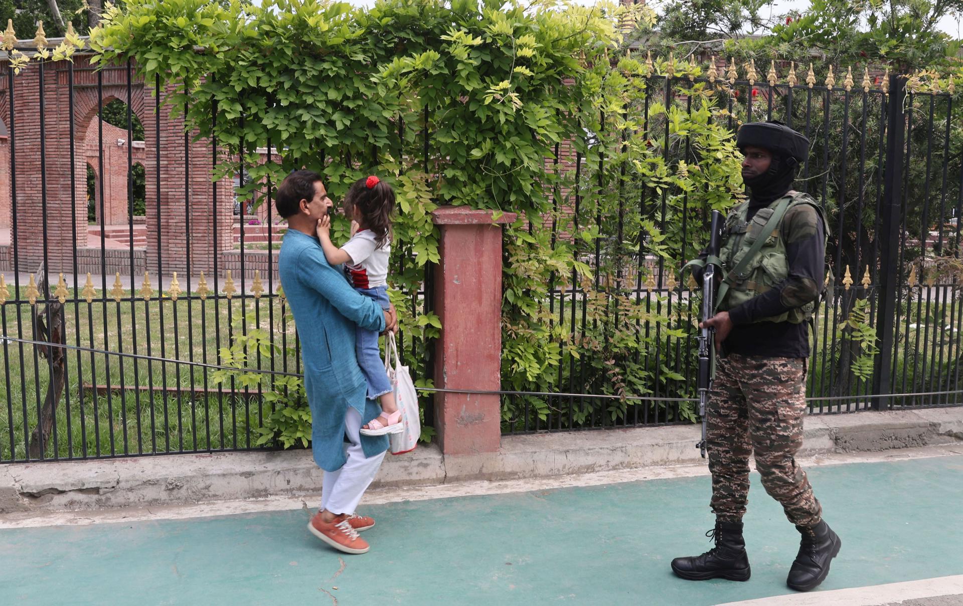 Un hombre camina con una niña en brazos junto a un soldado paramilitar indio en la ciudad cachemir de Srinagar. EFE/EPA/Farooq Khan