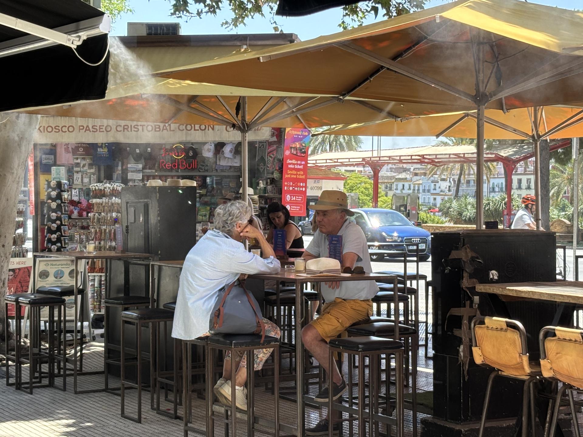 Unas personas en una terraza refrescada con aspersores, este miércoles con alta temperaturas en Sevilla. EFE/Carlos Rivera
