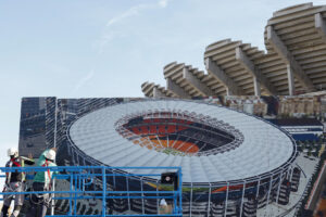 Dos operarios colocan un cartel con la imagen que presentará el Nou Mestalla junto al estadio en el que se han retomaron las obras, el pasado 10 de enero. EFE/Ana Escobar