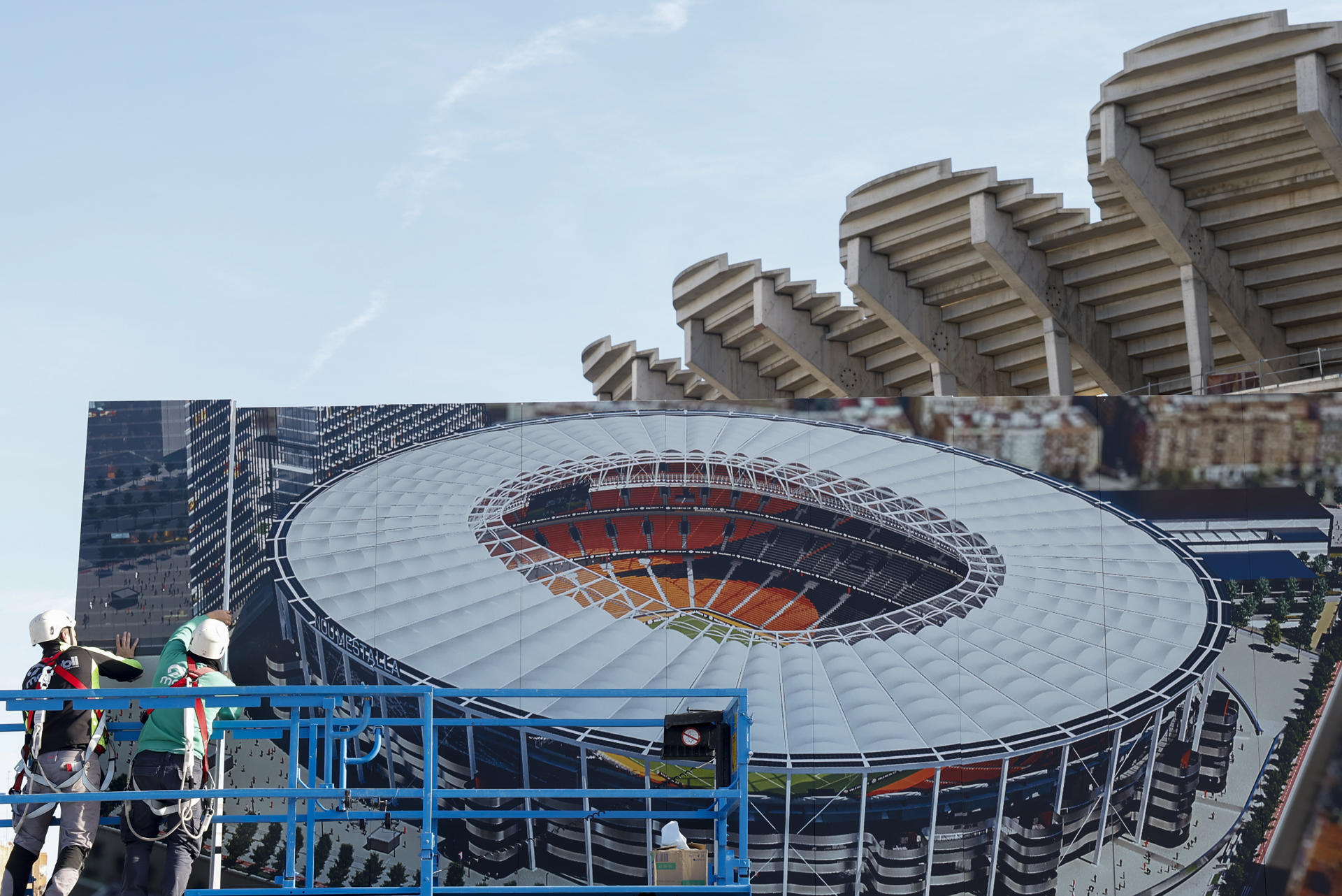 Dos operarios colocan un cartel con la imagen que presentará el Nou Mestalla junto al estadio en el que se han retomaron las obras, el pasado 10 de enero. EFE/Ana Escobar