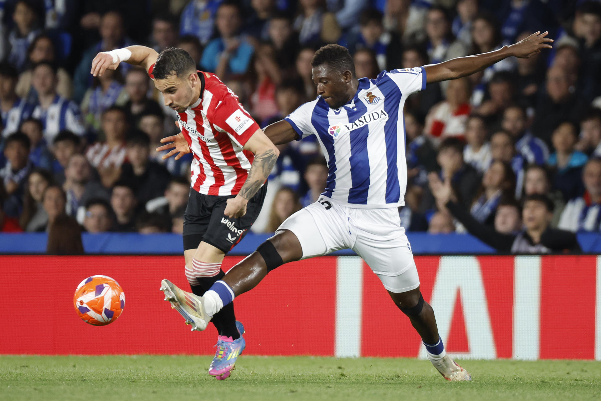 El defensa maliense de la Real Sociedad Hamari Traoré (d) pelea un balón ante el extremo del Athletic Álex Berenguer, durante el partido de LaLiga EA Sports de fútbol que Real Sociedad y Athletic Club disputaron en el Reale Arena, en San Sebastián. EFE/Juan Herrero