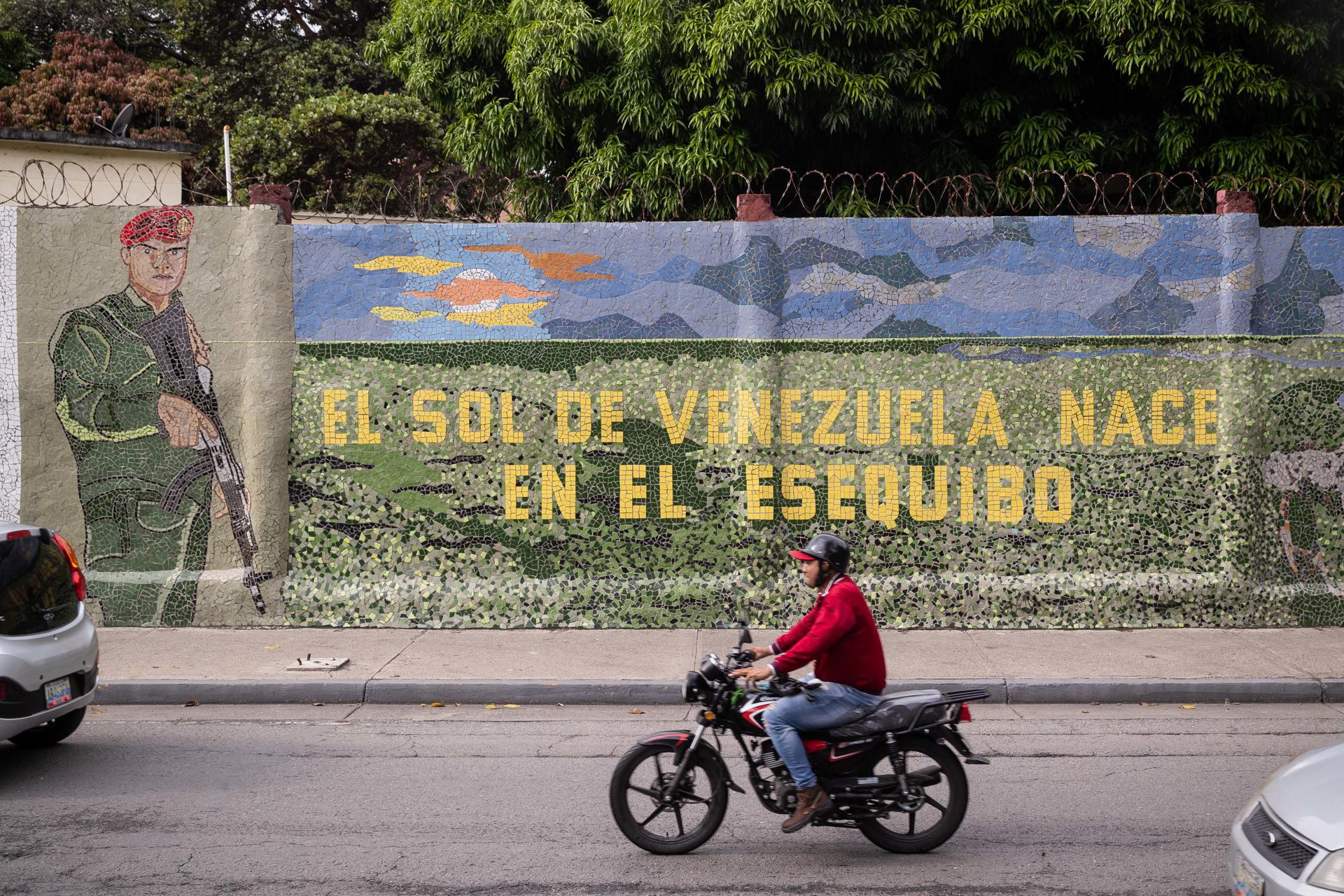 Fotografía de archivo de un hombre que conduce una moto frente a un mural que dice "El sol de Venezuela nace por el esequibo". EFE/ Rayner Peña R.