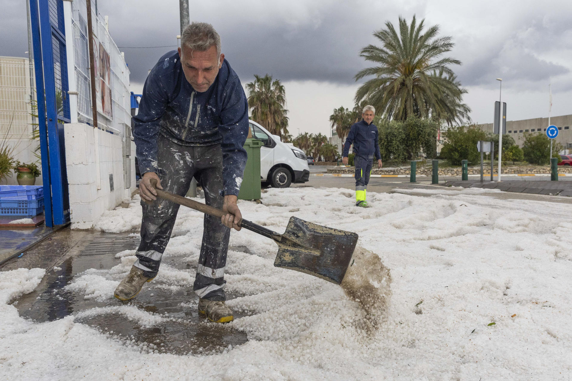 Un hombre retira el granizo de la puerta de su empresa este jueves en el Polígono Industrial de El Arreaque del municipio de Mula, tras la tormenta de granizo que ha caído en los municipios de Mula, Bullas, Calasparra y Cehegín. La autovía del noroeste se ha cortado un tiempo un carril por sentido hasta que el granizo acumulado ha sido retirado con quitanieves autonómicos. EFE/Marcial Guillén