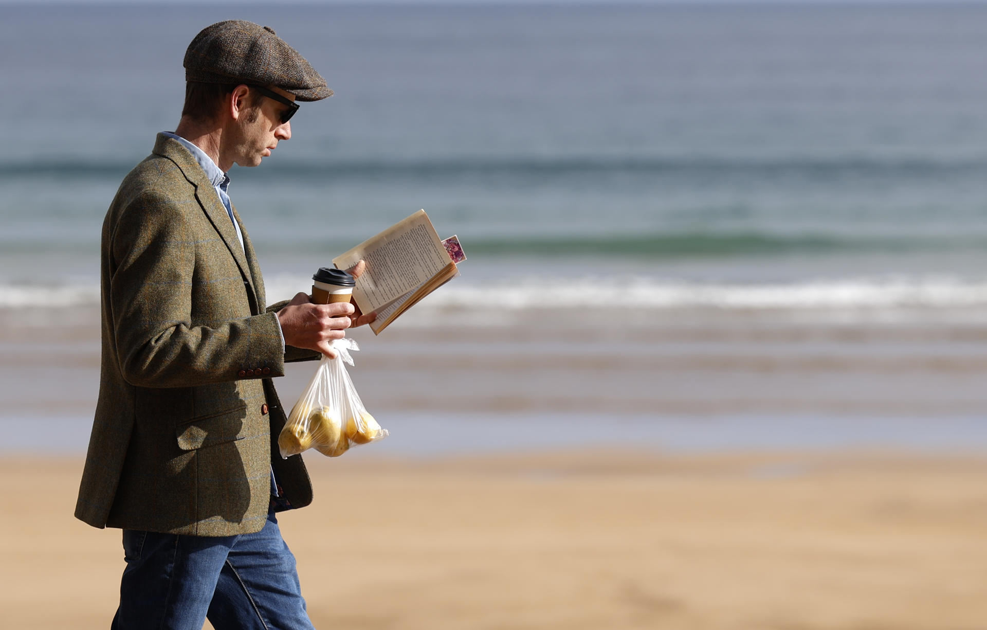 Un hombre pasea este domingo con un libro por el malecón de la playa guipuzcoana de Zarautz (Gipuzkoa). EFE/Juan Herrero.