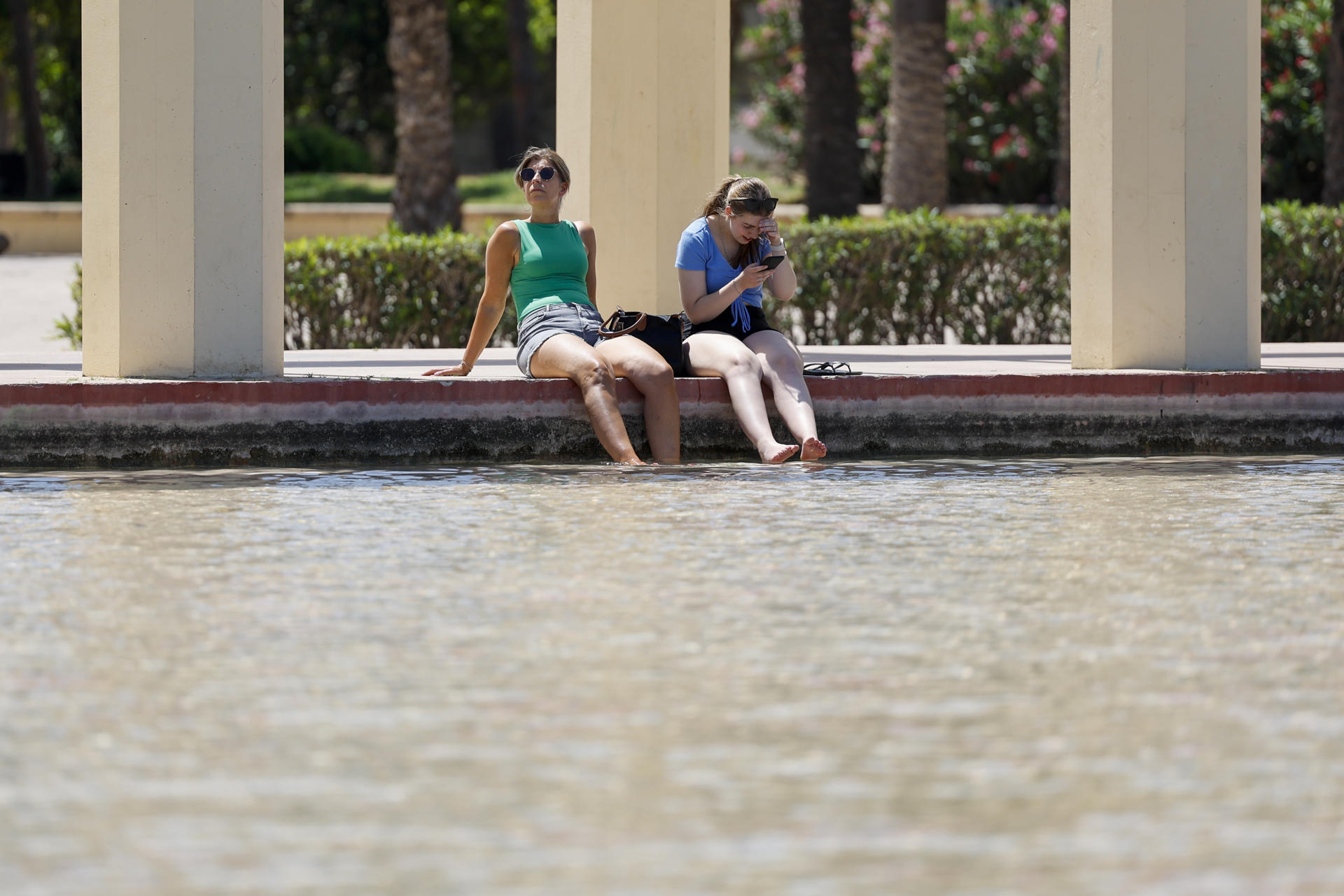 Dos personas se refrescan en una fuente de los jardines del antiguo cauce del Turia para combatir el calor que vive durante este lunes. EFE/Ana Escobar