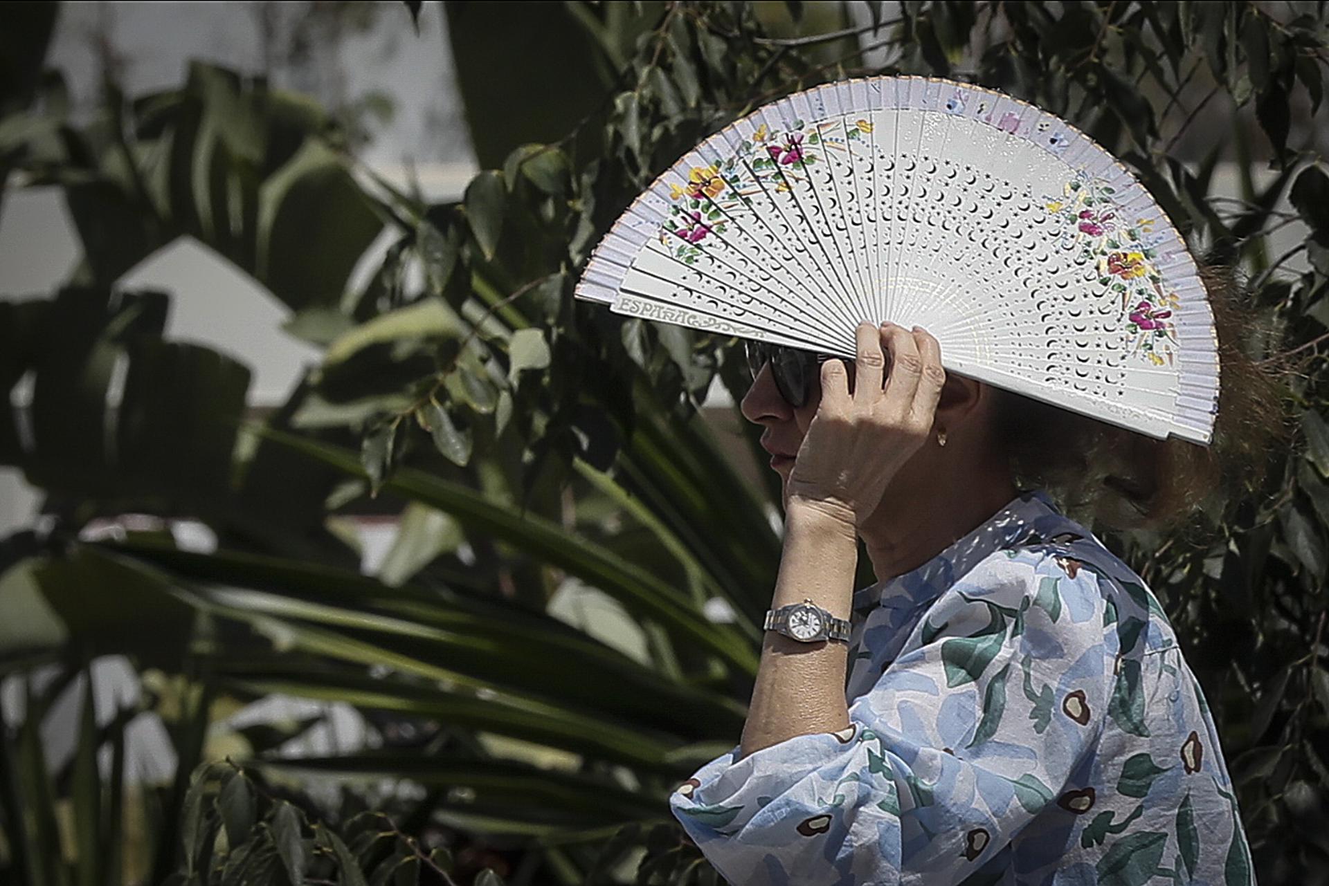 Una persona se cubre la cabeza con un abanico para paliar los rayos del sol directos mientras camina por Sevilla, en una fotografía de archivo. EFE/José Manuel Vidal