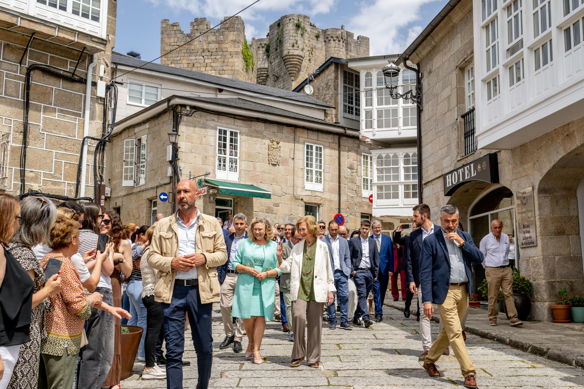 La reina emérita Sofía, acompañada por la alcaldesa de la localidad, Sara Inés Vega (c-i), saluda a los asistentes mientras visita Castro Caldelas (Ourense) este viernes como parte de una iniciativa de su Fundación orientada a promover el valor sostenible del medio rural y su patrimonio cultural y natural. EFE/ Brais Lorenzo