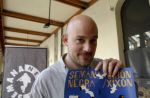 El director de la Semana Negra de Gijón, Miguel Barrero, posa con el cartel de la próxima edición este sábado durante la presentación de un avance de la programación. EFE/Juan González.
