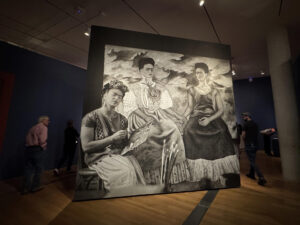Personas caminan cerca de una fotografía de la artista mexicana Frida Kahlo pintando su obra 'Las dos Fridas' (1939), durante su visita a  la muestra "Frida más allá del mito" el 24 de mayo de 2025 en el Museo de Bellas Artes de Virginia (VMFA) en Richmond, Virginia (EE.UU.). EFE/Yeny García