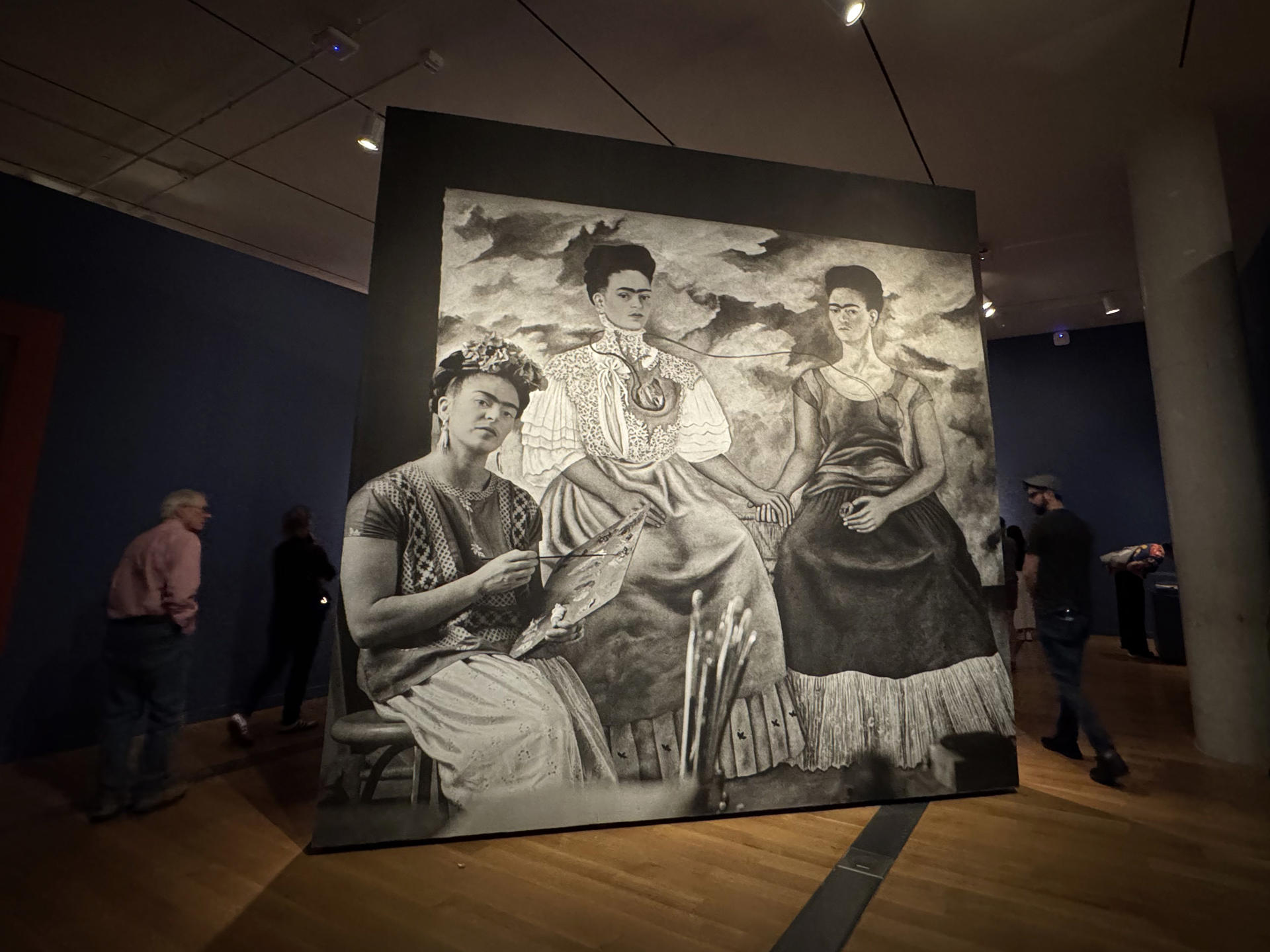 Personas caminan cerca de una fotografía de la artista mexicana Frida Kahlo pintando su obra 'Las dos Fridas' (1939), durante su visita a  la muestra "Frida más allá del mito" el 24 de mayo de 2025 en el Museo de Bellas Artes de Virginia (VMFA) en Richmond, Virginia (EE.UU.). EFE/Yeny García