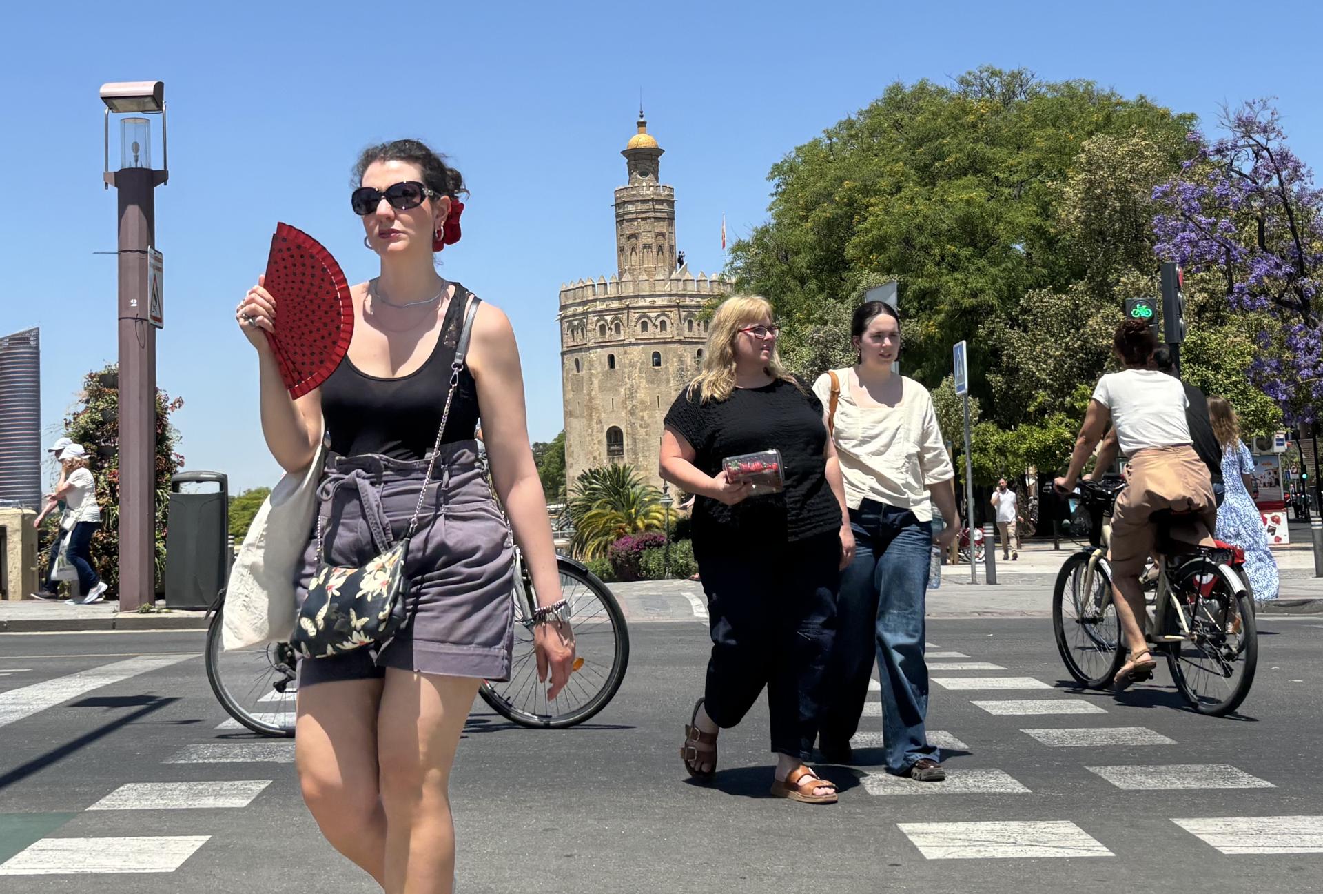 Varias personas caminan cerca de la Torre del Oro de Sevilla, este miércoles con alta temperaturas. EFE/Carlos Rivera