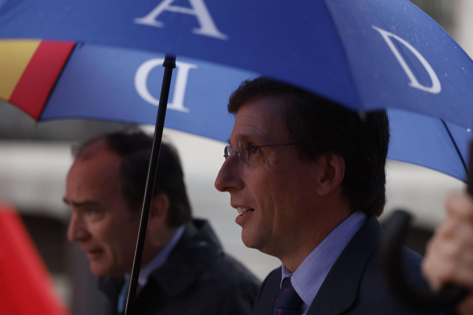 El alcalde de Madrid José Luis MArtínez-Almeida se protege de la lluvia con un paraguas mientras espera el comienzo del homenaje a los Héroes del 2 de Mayo en Madrid, este viernes. EFE/ Juan Carlos Hidalgo