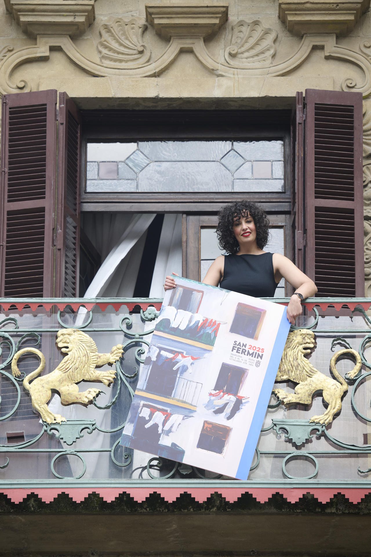 La pamplonesa Sandra Nadal posa para los gráficos con "Hogar pamplonica", el cartel que anunciará los Sanfermines de 2025, una imagen realista "de lo cotidiano, de lo doméstico, de lo que nos pertenece", de la fachada de una vivienda de cuyos balcones cuelgan las ropas blancas y complementos rojos típicos del atuendo festivo. EFE/Iñaki Porto