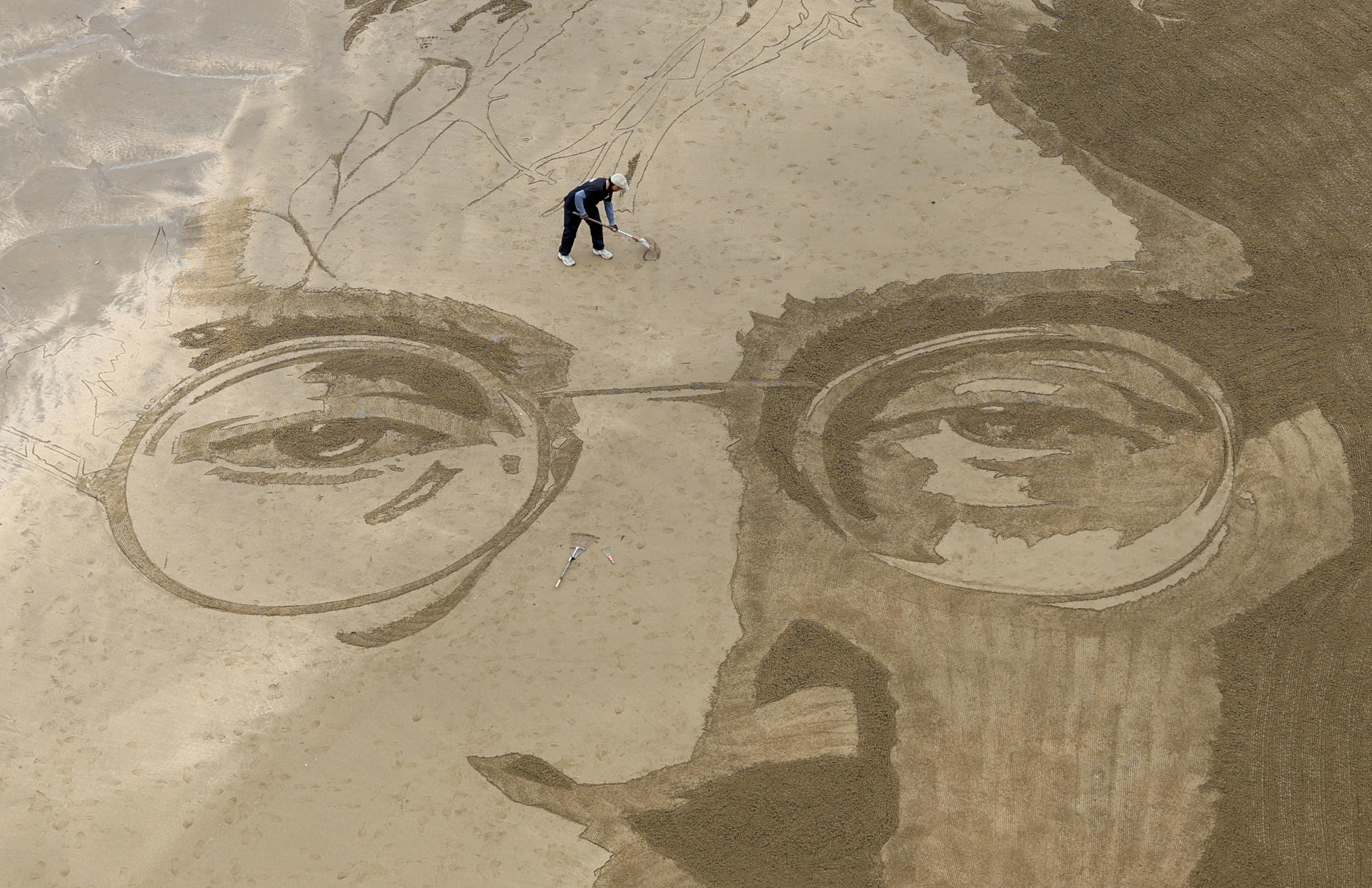 El arte efímero del peruano Germán Cedano se borra con la marea. Sus monumentales dibujos sobre la arena transforman la playa de La Concha de San Sebastián en un lienzo en el que este artista callejero graba retratos, mandalas y mensajes que se viralizan en redes y que, pese a su repercusión, nunca repite. En la imagen trabaja en un retrato del músico John Lennon creado en la playa de Itzurun de Zumaia (Gipuzkoa). EFE/Juan Herrero.
