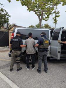 Fotografía cedida por la Oficina Federal de Investigaciones (FBI) donde aparece uno de sus agentes acompañado por un agente del Servicio de Inmigración y Control de Aduanas (ICE) custodiando a un inmigrante a una furgoneta en el condado de Los Ángeles, California (EE.UU.). EFE/FBI Los Ángeles