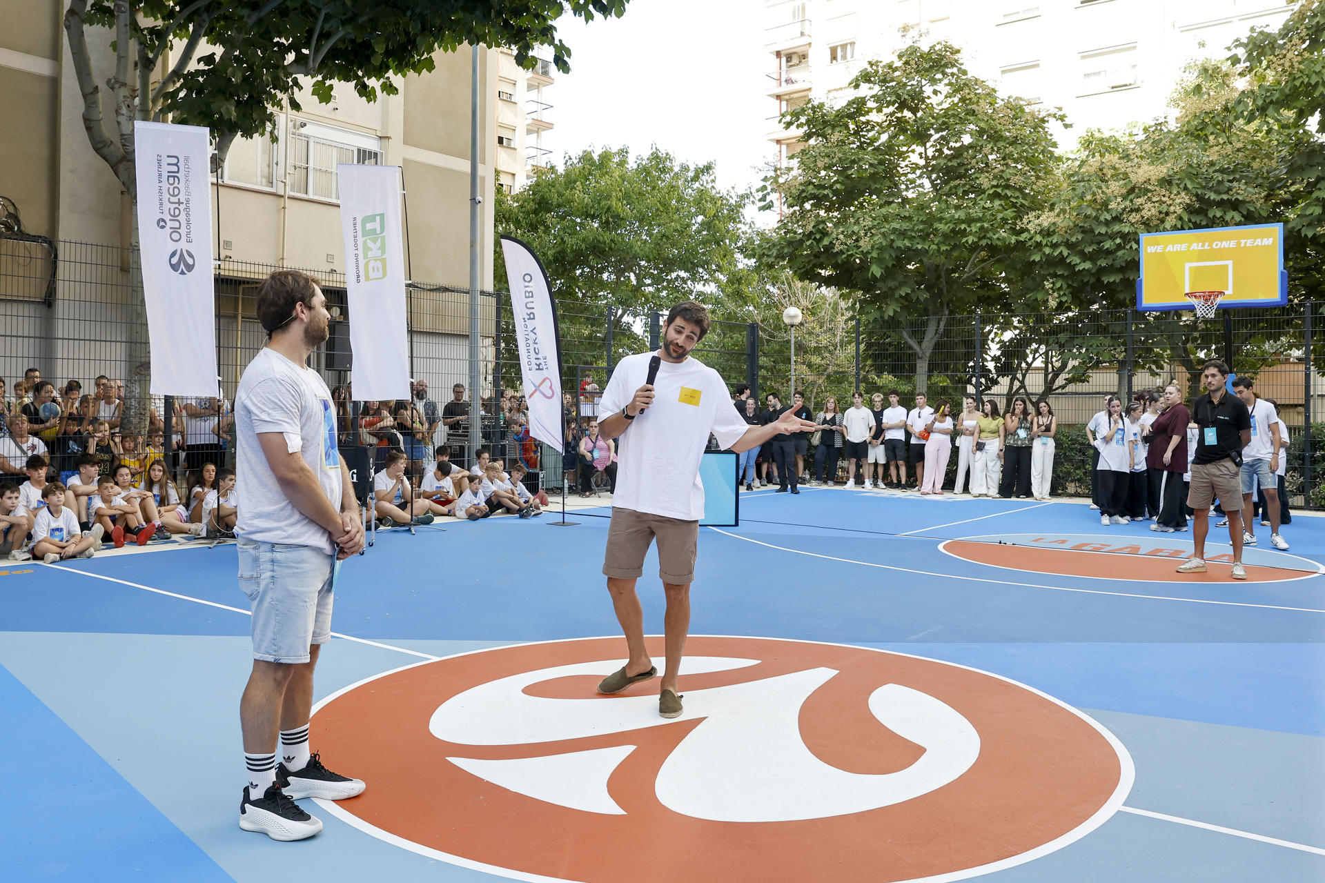 El jugador Ricky Rubio (c) participa este martes, en el acto de inauguración de una popular pista urbana de baloncesto ubicada en el barrio badalonés de Canyadó, que ha sido reformada gracias a un proyecto de la Euroliga y BKT con la colaboración de la Ricky Rubio Foundation. EFE/ Andreu Dalmau