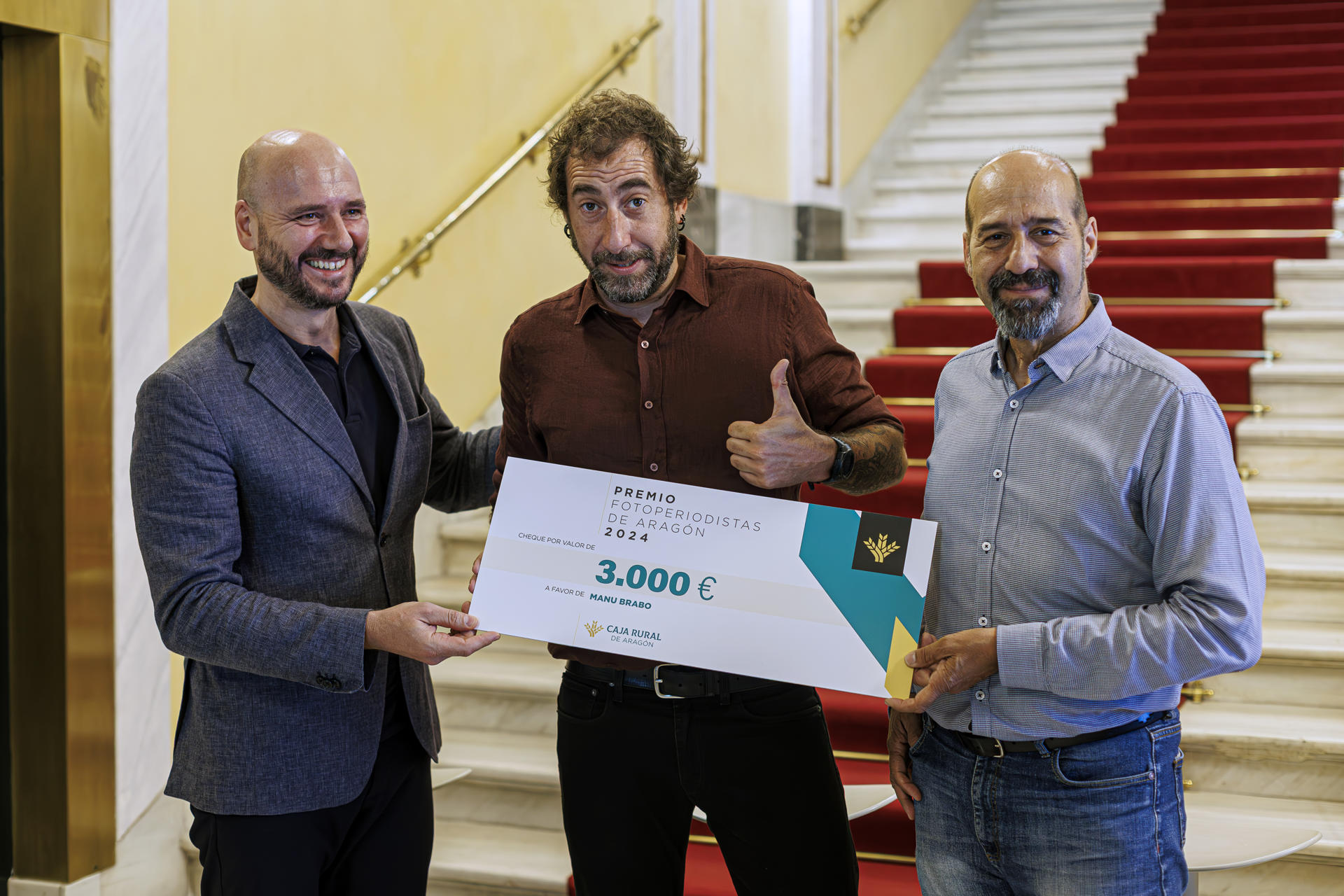 El fotoperiodista Manu Brabo (c), posa junto a Iñigo Martinez (i), Director de Comunicación de Caja Rural y Javier Cebollada (d), Presidente de Fotoperiodistas Aragón, este viernes en Zaragoza donde recoge el Premio Fotoperiodistas de Aragón 2024, como reconocimiento a su trabajo durante años en la guerra de Ucrania.-EFE/ Javier Belver
