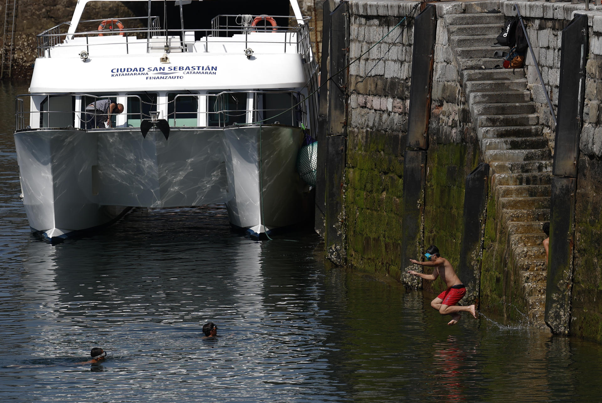 Unos jóvenes se bañan en el puerto pesquero de San Sebastián. EFE/Juan Herrero.