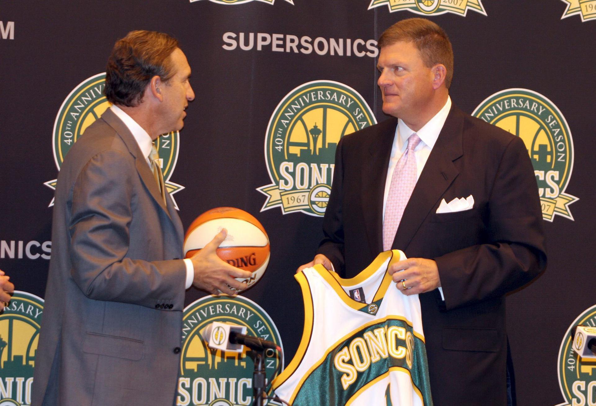 Fotografía tomada el 18 de julio de 2006 a Howard Schultz (i), entonces presidente del club de baloncesto de Seattle (BCOS) cuando entregaba una camiseta de los SuperSonics y un balón al inversionista Clayton Bennett (d), tras el anuncio de venta del equipo de la NBA al grupo de inversión que estableció la franquicia en Oklahoma City, la ciudad que ese dominco celebra la conquista del primer anillo. EFE/Dan Levine