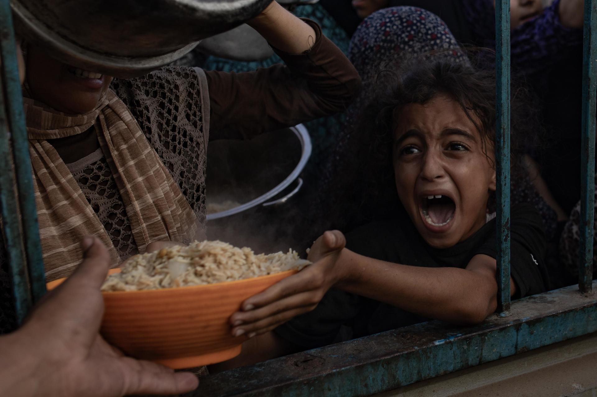Una niña palestina desplazada interna trata de recoger alimentos.EFE/EPA/HAITHAM IMAD