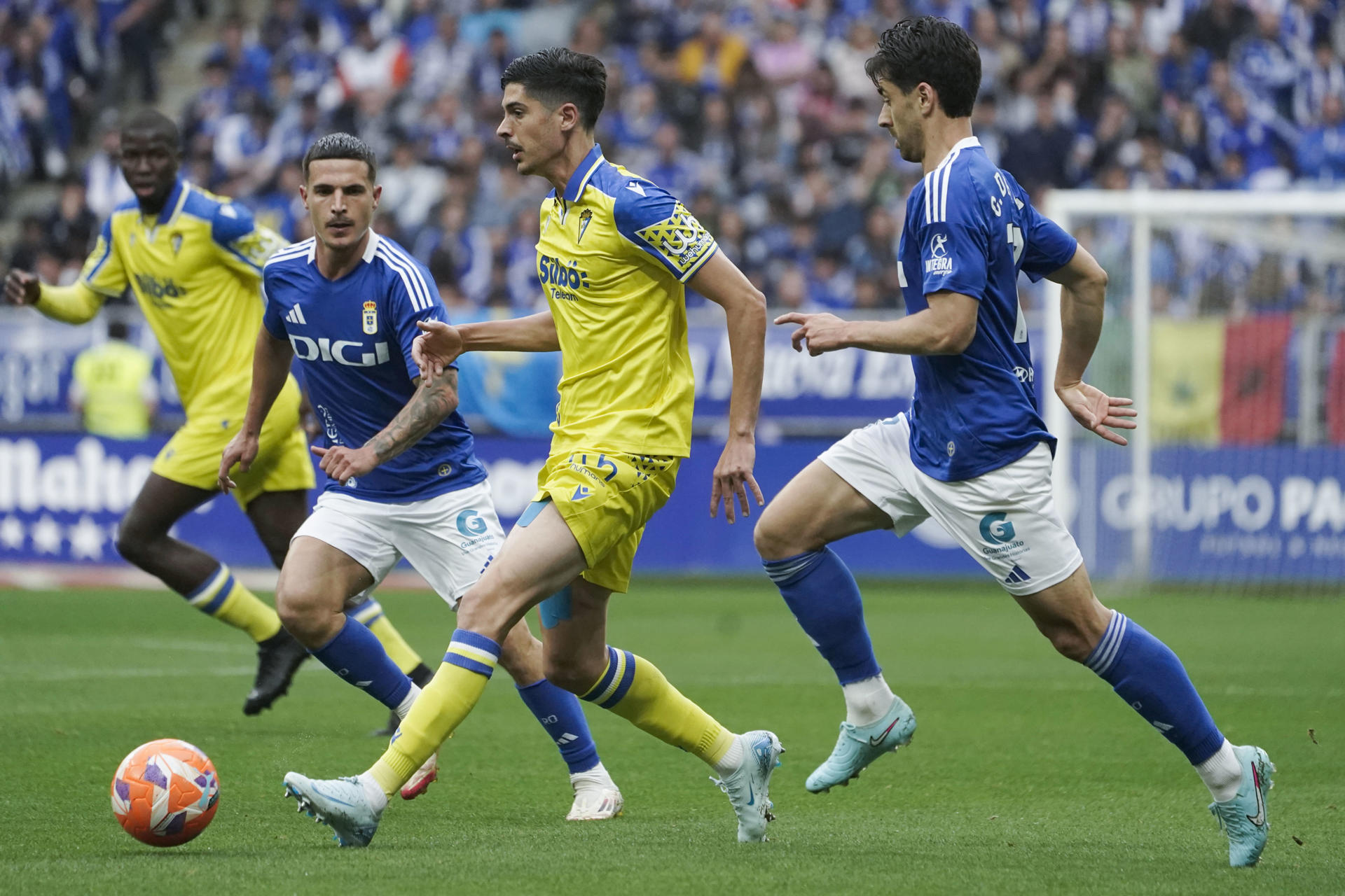 El delantero del Cádiz, Carlos Fernández (c), se lleva el balón ante los jugadores del Oviedo durante el encuentro correspondiente a la última jornada de la Liga Hypermotion que disputan hoy domingo Real Oviedo y Cádiz en el estadio Carlos Tartiere de la capital asturiana. EFE/Paco Paredes.
