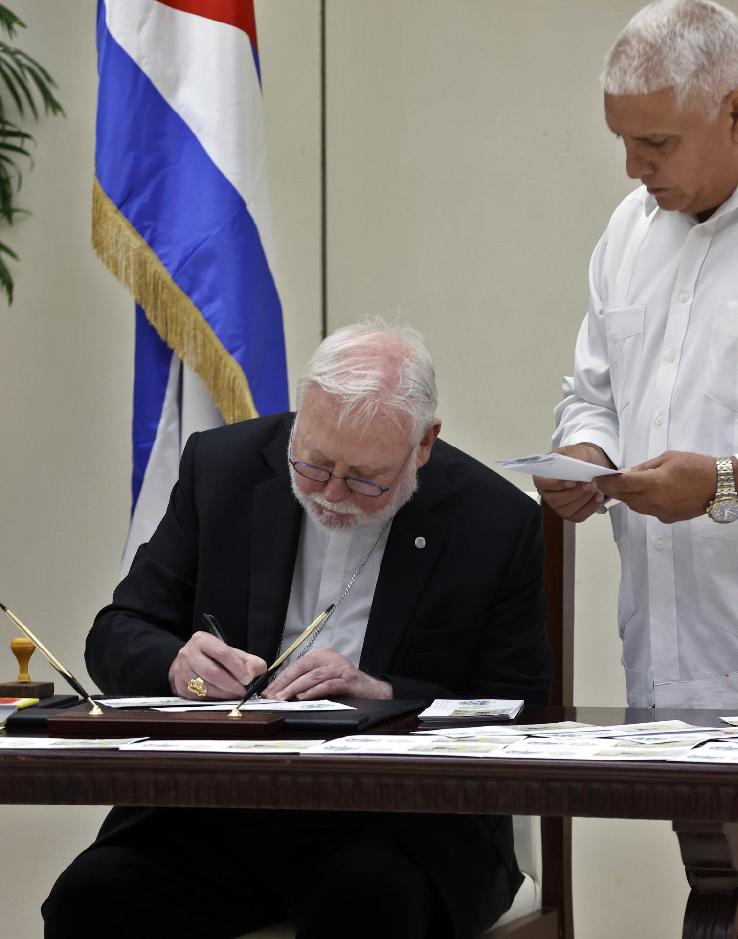 El secretario del Vaticano para las Relaciones con los Estados y los Organismos Internacionales, Paul Richard Gallagher (i), asiste a la cancelación de un sello postal que conmemora los 90 años de relaciones de Cuba con el Vaticano este 4 de junio de 2025, en La Habana (Cuba). EFE/ Ernesto Mastrascusa
