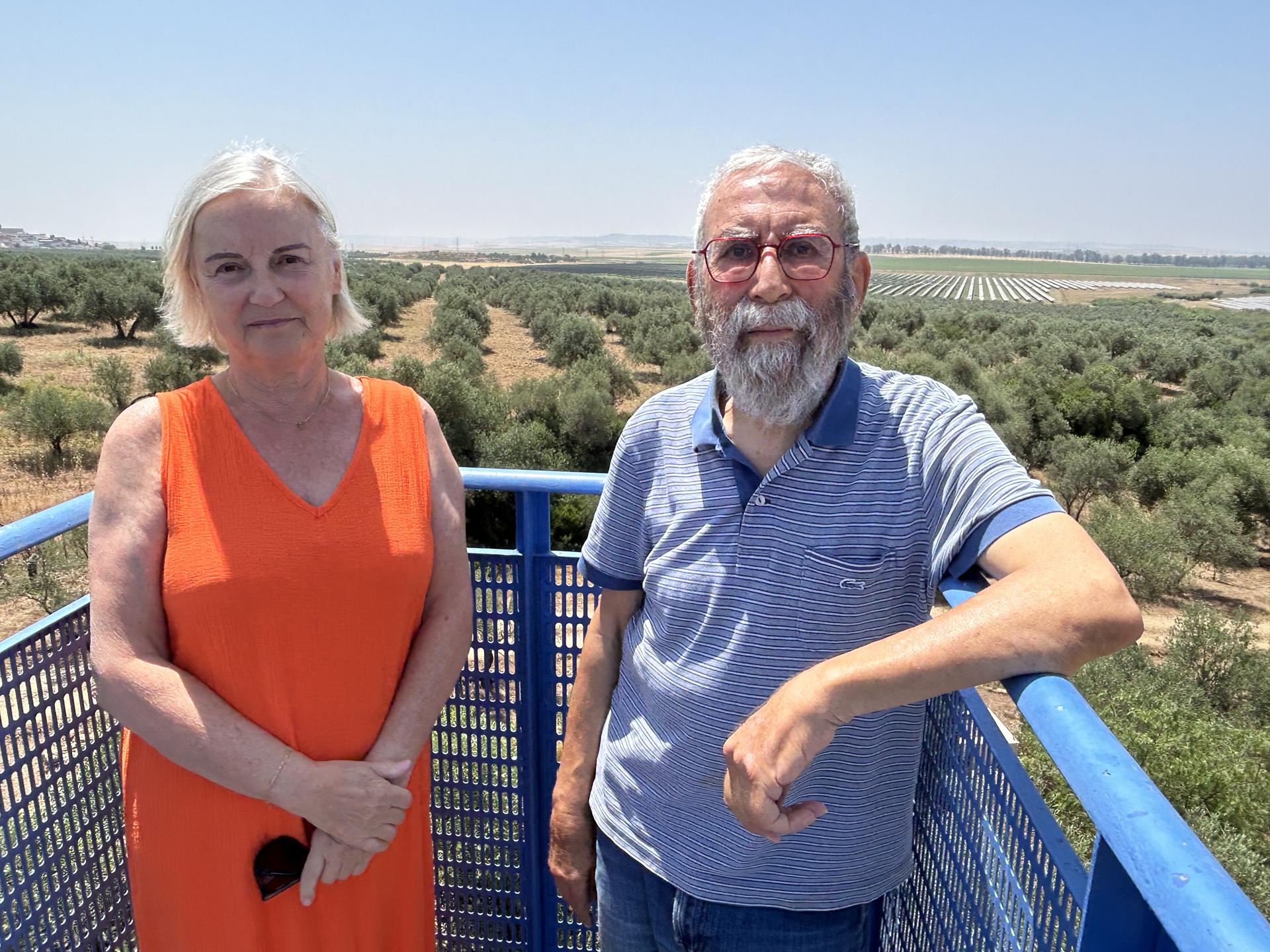 Nieves González y Carlos Ortega son una pareja que viven en una casa en el municipio de Gerena (Sevilla) y posan en un balcón con la imagen al fondo de los terrenos donde hay previsto el proyecto de un campo solar que rodeará su vivienda y les hará imposible vivir en ella, por lo que han comenzado un proceso para intentar paralizarlo. EFE/Fermín Cabanillas