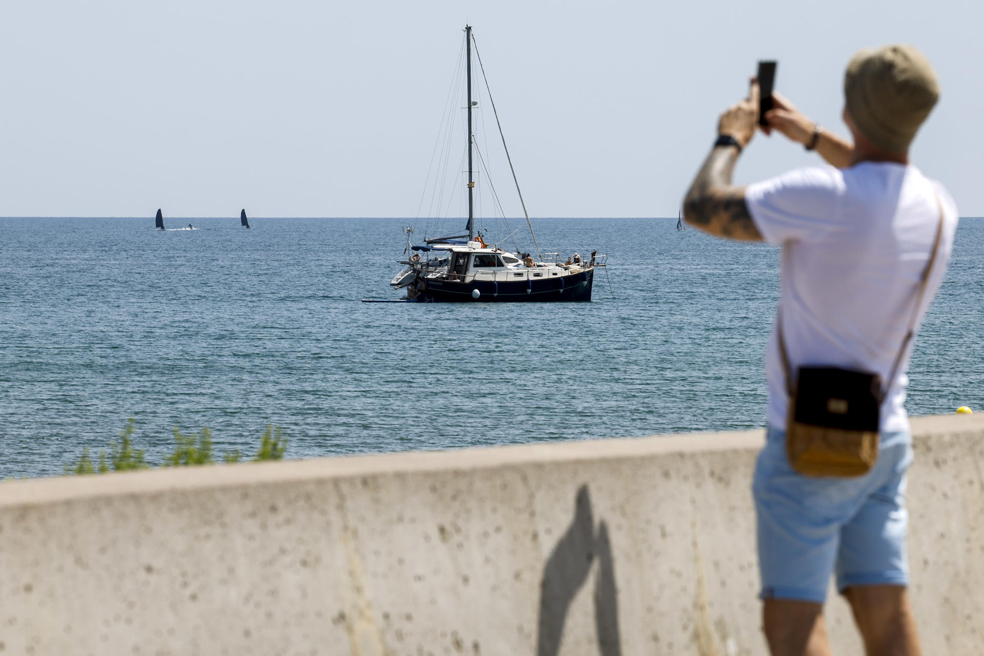 Un hombre saca una foto junto a un velero en la playa de la Malvarrosa en Valencia este lunes. EFE/ Ana Escobar