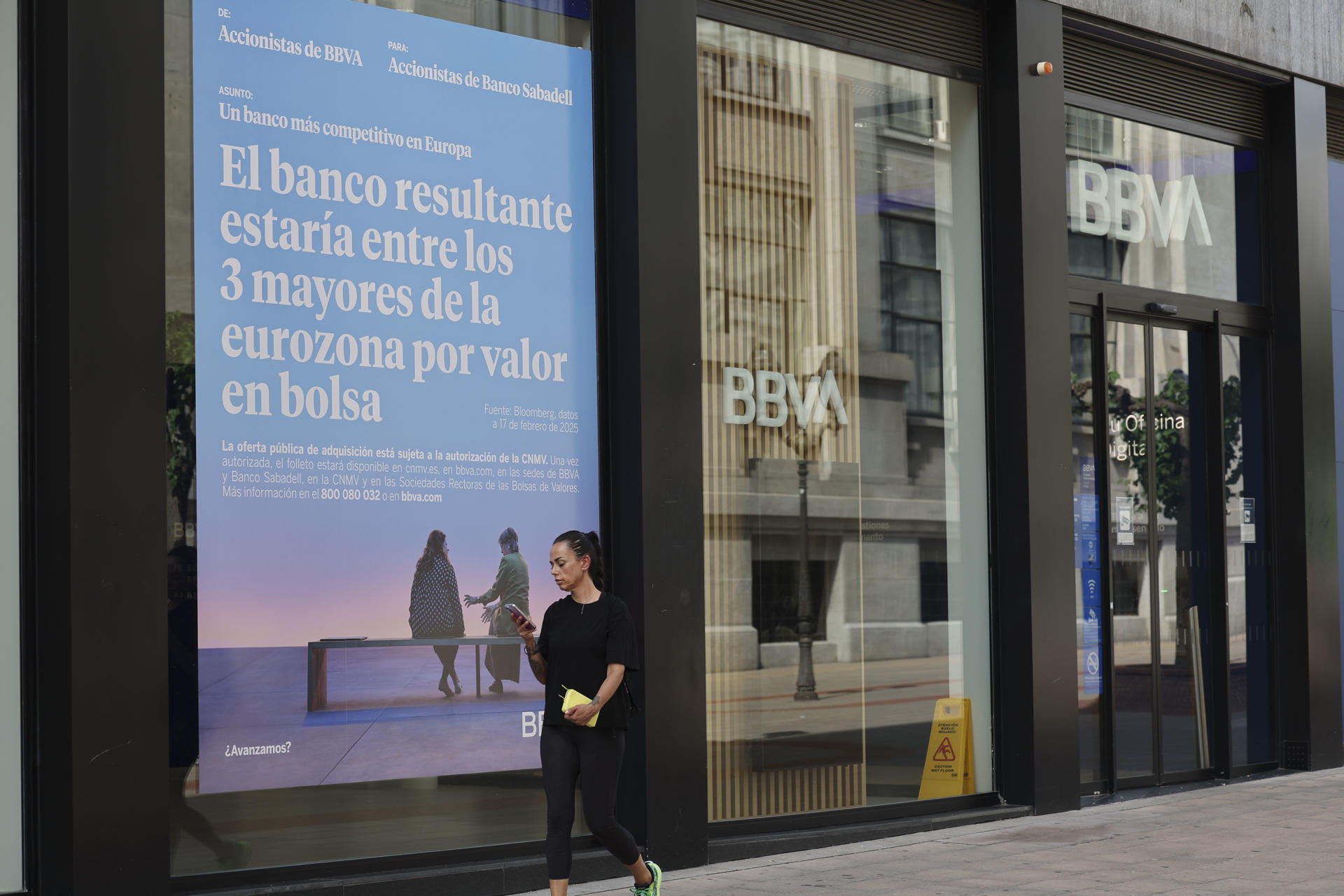 Un cartel en una sucursal del BBVA, en Bilbao este martes aludiendo a la fusión entre BBVA y Sabadell. La Comisión Europea recordó este martes que cualquier condición impuesta por un Gobierno para aprobar una transacción debería ser "excepcional, proporcionada y justificada por razones de interés público válidas", aunque rehusó pronunciarse en concreto sobre la decisión del Ejecutivo español respecto a la opa del BBVA por el Sabadell. EFE/Luis Tejido