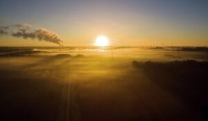 El sol se asoma en el horizonte al amanecer en un campo eólico con el humo de una fábrica de fondo, en una imagen de archivo. EFE/Julian Stratenschulte