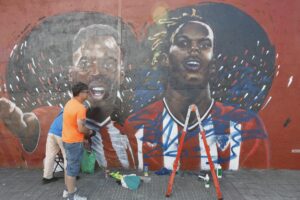 El mural con la imagen de Nico Williams en Barakaldo que había sido atacado el pasado fin de semana ha vuelto a ser vandalizado la pasada madrugada unas horas después de que el autor, el artista Carlos López (en la imagen), hubiese iniciado en la jornada del viernes los trabajos de restauración.
La figura de Nico ha sido emborronada con pintura azul y a su lado ha aparecido escrito 'rata de mierda', insulto que el propio López ha borrado nada más regresar al muro en la mañana del sábado para retomar su labor en el muro exterior de una parcela del barrio de Lutxana. Posteriormente ha continuado limpiando el resto de la pintura lanzada con spray con relativa facilidad mediante un trapo empapado en disolvente. EFE/ Miguel Toña