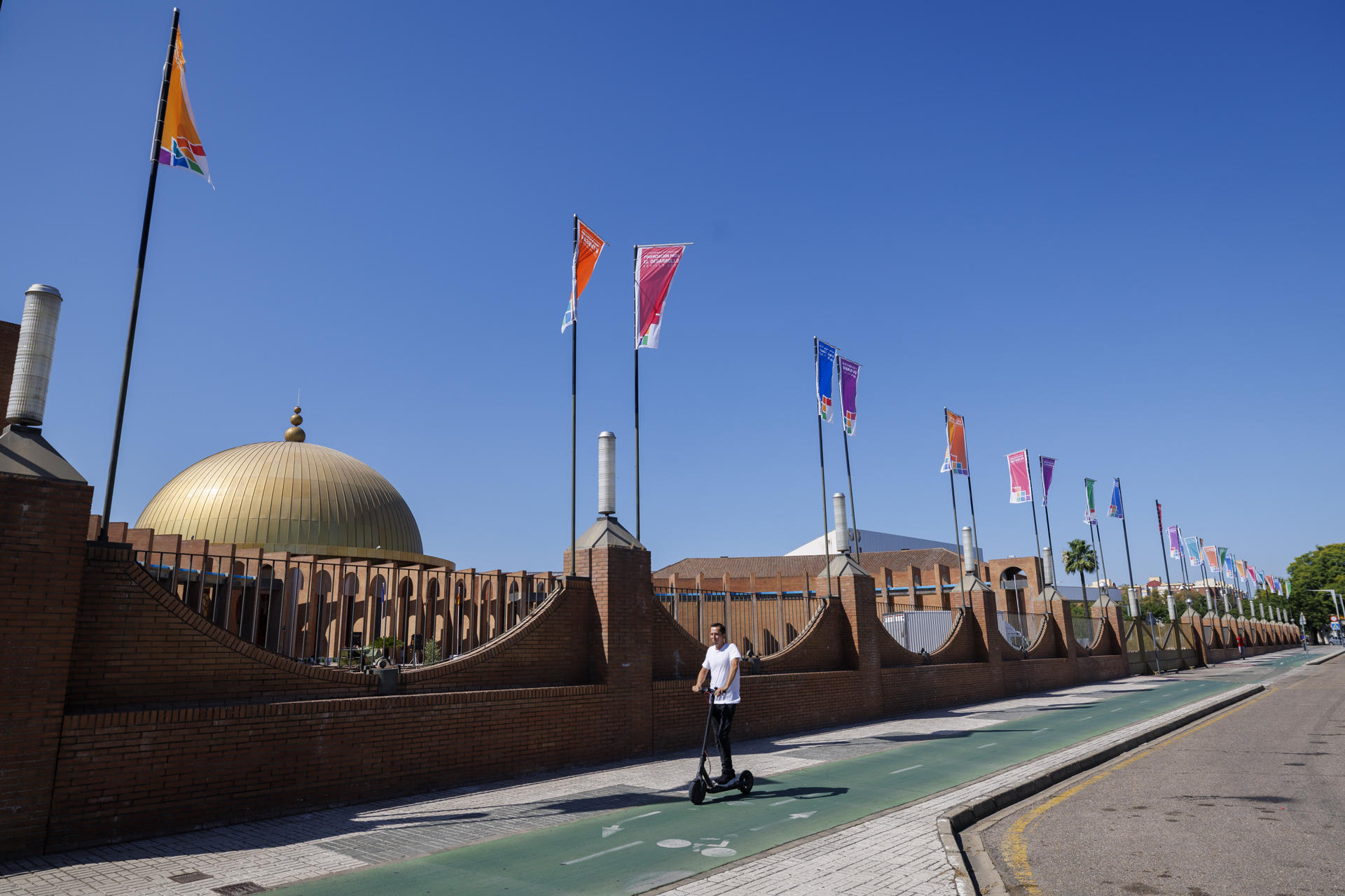 Una persona en patinete circula junto al Palacio de Congresos FIBES de Sevilla este viernes. La IV Conferencia Internacional sobre Financiación para el Desarrollo (FFD4), que acogerá Sevilla a partir del próximo lunes hasta el 3 de julio, se suma a las grandes citas de relevancia mundial, como la Exposición Iberoamericana de 1929 o la Expo'92, que la capital de Andalucía ha albergado a lo largo de su historia. EFE/ Julio Muñoz
