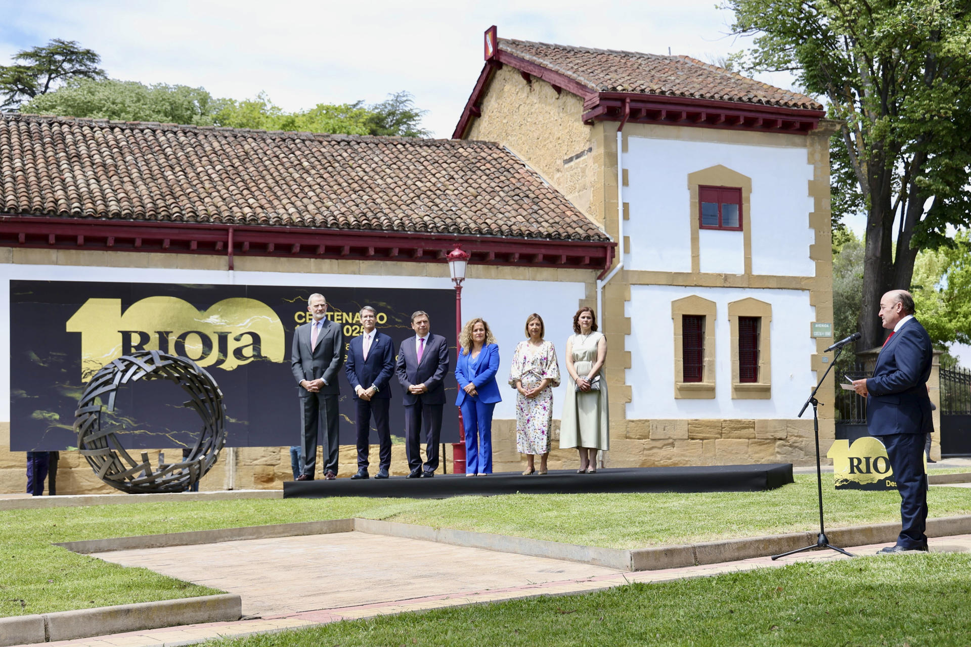El rey Felipe VI ha inaugurado este jueves, en la ciudad riojana de Haro, el nuevo ‘Espacio Centenario de Rioja’ y la escultura ‘Somos tiempo’, obra del artista José A. Olarte, que conmemora los cien años de la Denominación de Origen Calificada (DOCa) Rioja y que refleja una esfera inacabada. En la imagen, escuchan la intervención del presidente del Consejo Regulador, Fernando Ezquerro (d) EFE/Raquel Manzanares
