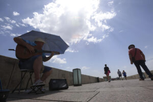 Un músico callejero se protege con una sombrilla de las altas temperaturas mientras toca en el Puente Romano de Córdoba. .EFE/Salas