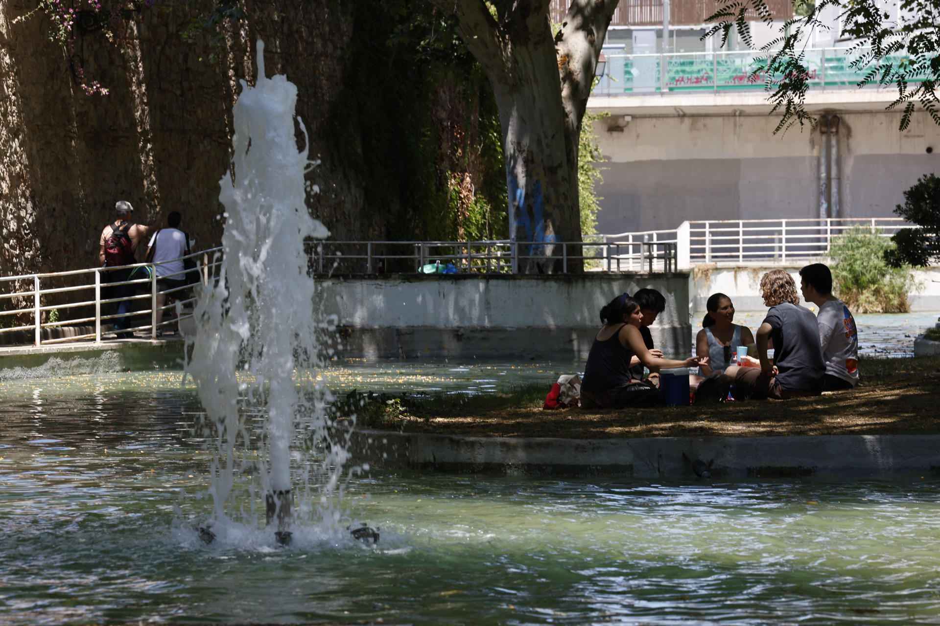 Unos jóvenes se reúnen bajo la sombra de un árbol y al lado de una fuente en el parque de la España Industrial en el barrio de Sants en Barcelona este domingo. Cataluña afronta este domingo el segundo día de la primera ola de calor de 2025, que en principio se prolongará hasta el martes, tras una noche tórrida que ha dejado una mínima de 30,4 grados en Portbou (Girona) y de 28 en Barcelona, según los registros del servicio Meteocat. Una ola de calor en la que ayer se registraron 46 grados en El Granado (Huelva), un hecho que nunca se había dado en el mes de junio, ha informado la Agencia Estatal de Meteorología (Aemet) este domingo. EFE/ Toni Albir