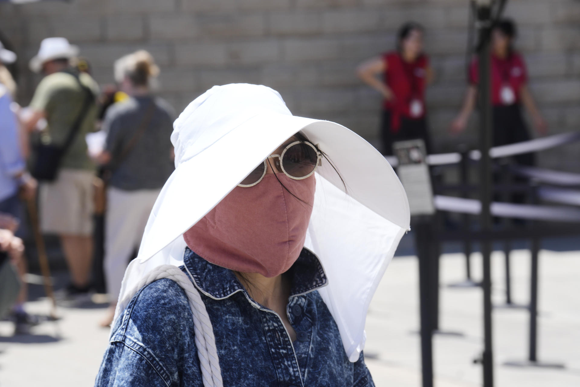 Una turista utiliza un sombrero y una mascarilla para protegerse del sol frente a la Sagrada Familia en Barcelona este sábado. Catorce comunidades están este sábado en alerta por temperaturas excepcionalmente altas en el día de inicio de la primera ola de calor del verano en España. EFE/ Alejandro García