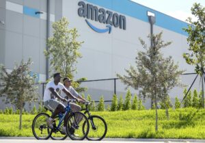 Fotografía de archivo de dos personas circulando en bicicleta frente a un centro logístico de Amazon en Florida (EE.UU.). Zoox, la empresa de vehículos autónomos propiedad de Amazon, inauguró una planta que se centrará en la producción de robotaxis en California, con la que busca hacer competencia a Waymo, según apuntan este miércoles los medios locales. EFE/EPA/ CRISTOBAL HERRERA-ULASHKEVICH / ARCHIVO