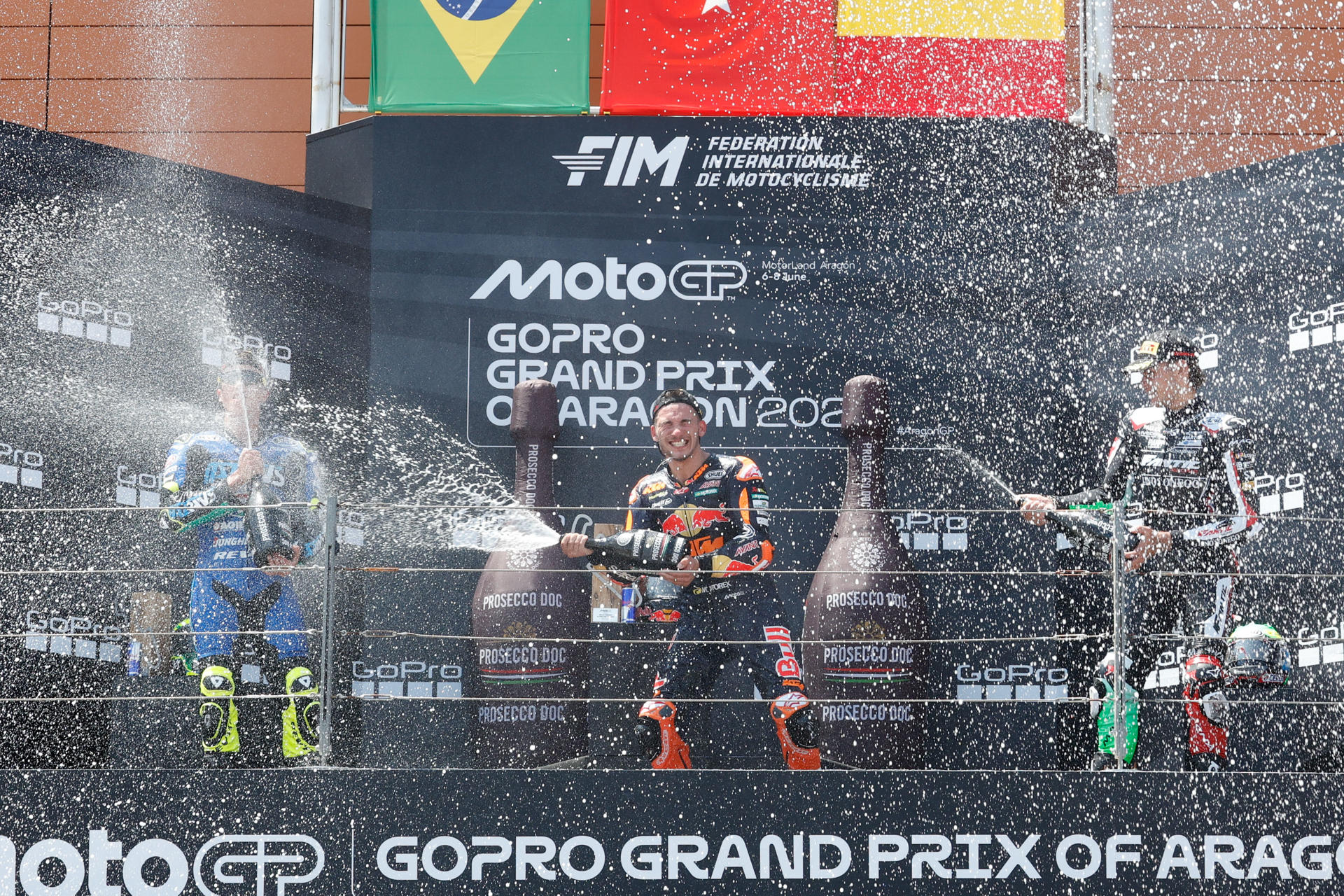 El ganador, el piloto turco Denis Öncü (d), del equipo Red Bull KTM Ajo, el segundo clasificado, el brasileño Diogo Moreira (i), de Italtrans Racing Team, y el tercer clasificado, el piloto belga Barry Baltus, del equipo Fantic Racing LINO SONEGO, en el podio de la carrera de Moto2 del Gran Premio de Aragón de MotoGP en el circuito Motorland de Alcañiz. EFE/Javier Cebollada