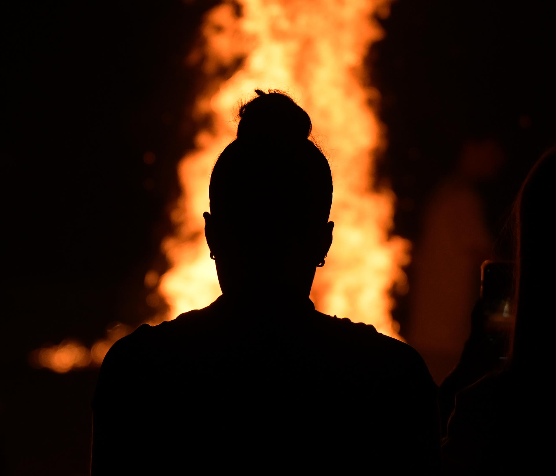 Silueta de una mujer observando una de las hogueras encendidas hoy lunes en la playa coruñesa de Riazor durante la celebración de la noche de San Juan. EFE / Moncho Fuentes.