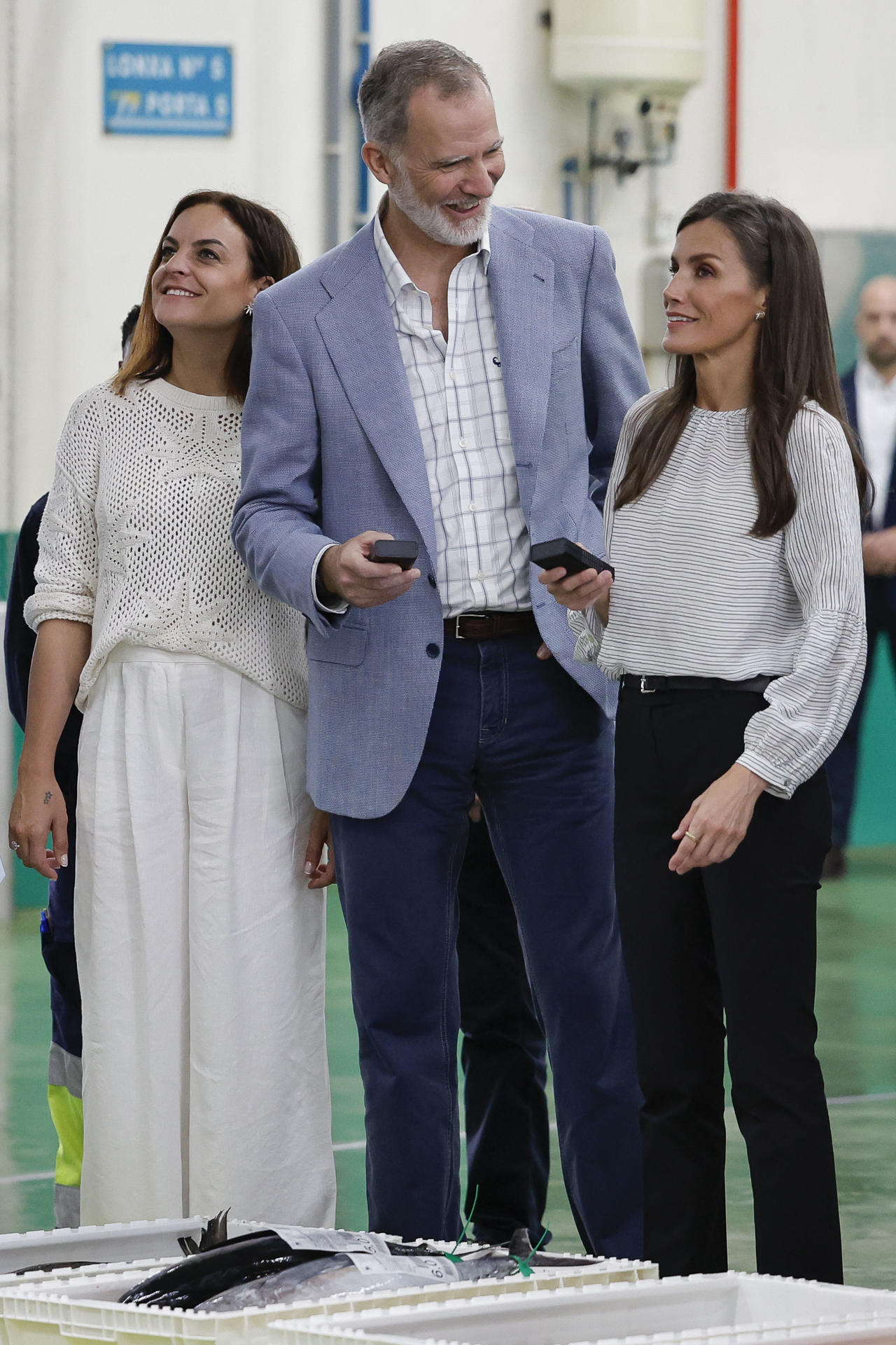 La reina Letizia (d) y el rey Felipe VI (c), participan en la subasta de la lonja de Burela (Lugo) acompañados por la alcaldesa de la localidad, Carmela López, durante su visita para interesarse de primera mano por la realidad del sector pesquero de A Mariña lucense. En Galicia se denomina "redeiras" a las mujeres que reparan las redes de pesca. EFE/ Lavandeira Jr.