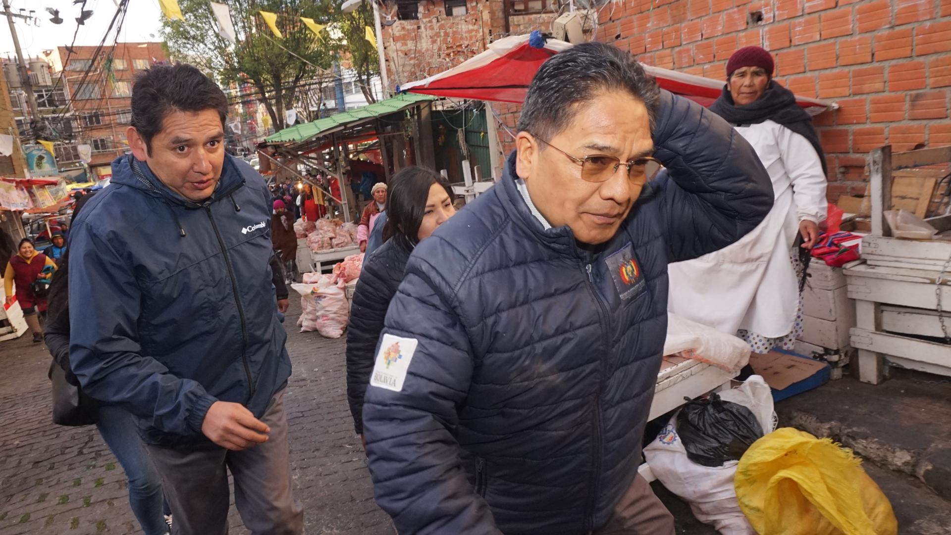 El viceministro boliviano de Defensa de los Derechos del Usuario y Consumidor, Jorge Silva (d), se retira de un mercado luego que ciudadanos lo increparan y le lanzarán frutas a la cabeza debido a la escasez de algunos productos, este miércoles en La Paz (Bolivia). EFE/Stringer