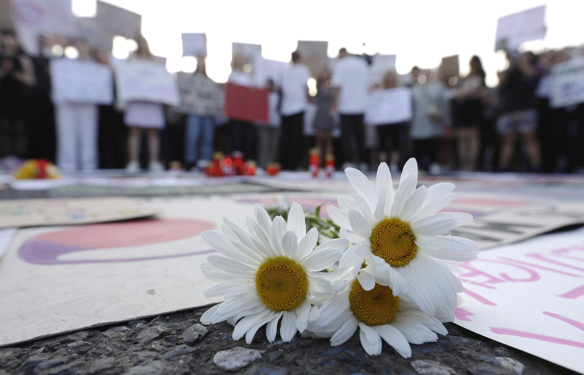 Detalle de un ramo de margaritas frescas sobre el pavimento y en medio de pancartas, durante una protesta por el asesinato de una joven embarazada, este miércoles, 18 de junio, frente a la sede del gobierno, en Bucarest (Rumanía) EFE/Robert Ghement
